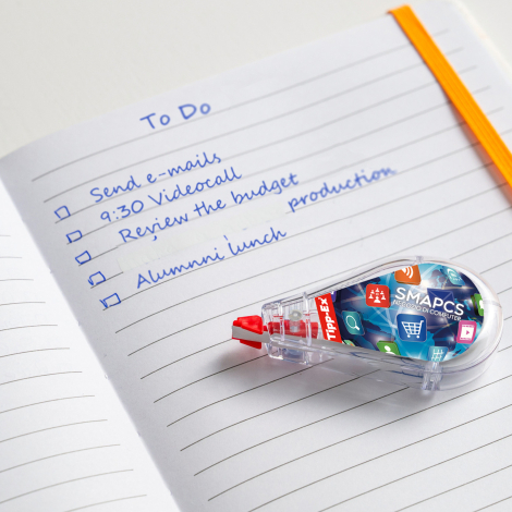 Correcteur Tipp-Ex Mini Pocket Mouse posé sur un cahier ouvert avec capot transparent et personnalisation visible sur la face la