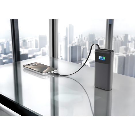 Batterie externe posée sur surface vitrée connectée à un smartphone avec vue urbaine en arrière-plan, sans personnalisation appa