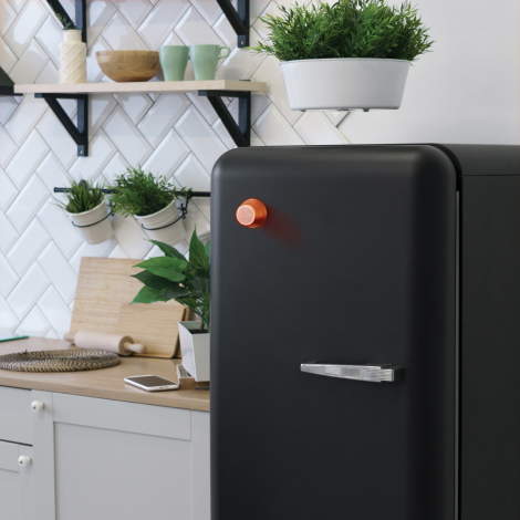 Haut-parleur fixé sur une porte de réfrigérateur en situation d’usage dans une cuisine, sans marquage visible