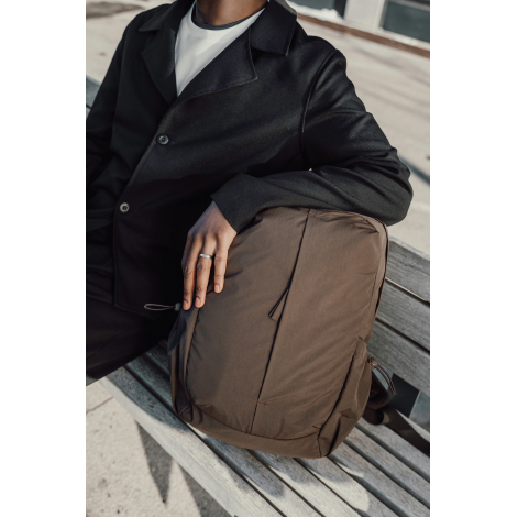 Sac à dos marron tenu par une personne assise sur un banc en situation d’usage, sans personnalisation apparente