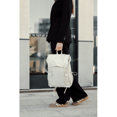Sac à dos beige porté à la main par une personne en extérieur, sans personnalisation visible