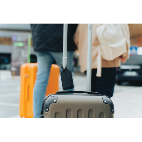 Étiquette fixée sur une valise en déplacement avec personnes en arrière-plan, sans marquage apparent