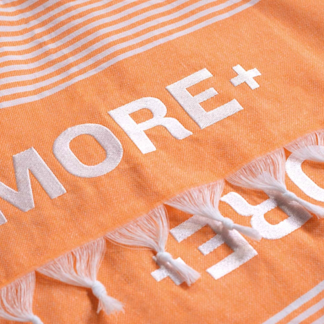Gros plan sur une serviette orange, avec un marquage texte en relief près des franges.