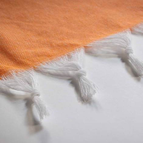 Zoom sur l’extrémité d’une serviette orange, mettant en avant les franges.