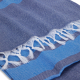 Serviette bleue vue en angle, avec un décor tissé en bandes horizontales et des franges visibles.
