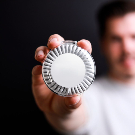 Boîtier rond blanc tenu en main par un homme montrant la surface extérieure, sans marquage visible.