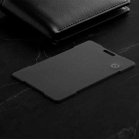 Traceur noir format carte posé sur une surface sombre à côté d’un portefeuille, sans marquage visible.