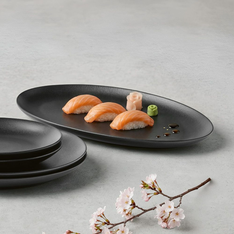 Plat ovale en céramique noire utilisé pour présenter des aliments avec d’autres assiettes empilées à proximité, sans personnalis