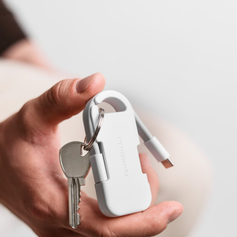 Powerbank blanche tenue en main avec câble intégré visible et clés attachées, sans marquage visible.