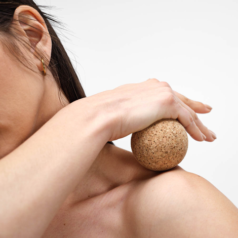 Sphère en liège utilisée en massage sur l’épaule d’une femme, sans personnalisation visible.