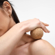 Sphère en liège utilisée en massage sur l’épaule d’une femme, sans personnalisation visible.