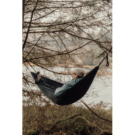 Hamac noir suspendu entre des arbres en extérieur, avec une personne allongée à l’intérieur, sans personnalisation visible sur l