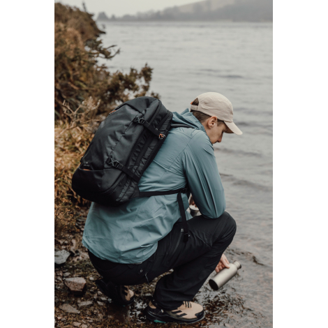 Sac à dos porté par une personne accroupie en extérieur, sans personnalisation visible.