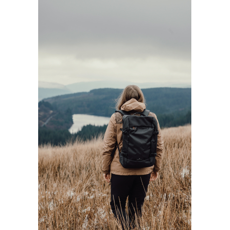 Sac à dos porté par une personne debout en extérieur vu de dos, sans personnalisation visible.