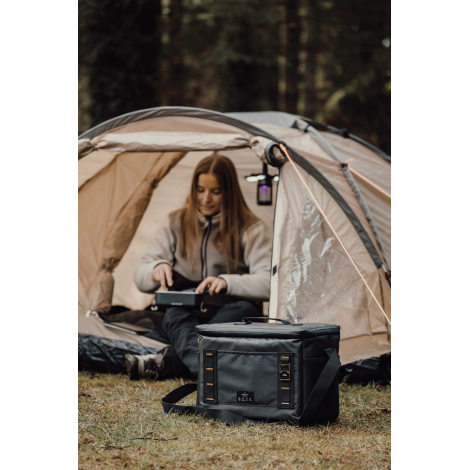 Personne assise devant une tente avec sac isotherme posé à proximité, sans marquage visible.