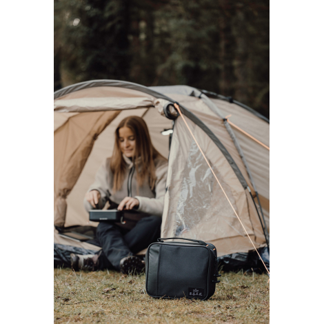Personne utilisant un sac isotherme en extérieur devant une tente, sans personnalisation visible.