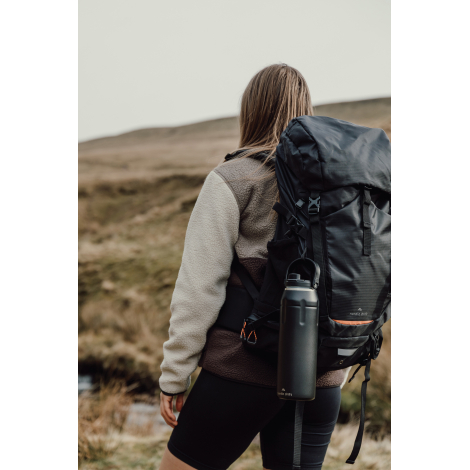 Bouteille fixée sur un sac à dos porté en extérieur, sans marquage visible.
