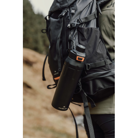Gourde fixée sur un sac à dos porté en extérieur, sans marquage visible.