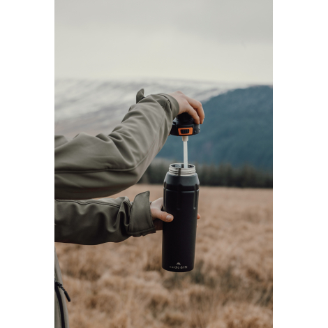 Personne ouvrant une gourde en extérieur, sans marquage visible.