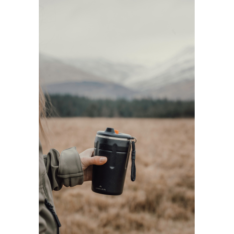 Personne tenant un gobelet isotherme en extérieur, sans marquage visible.