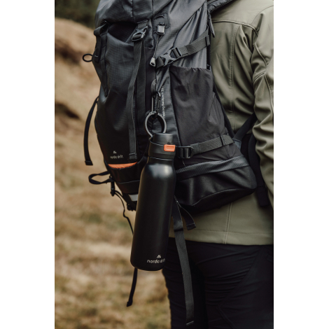 Gourde accrochée à un sac à dos porté en extérieur, sans marquage visible.