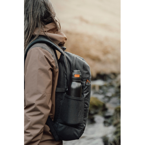 Gourde rangée dans une poche latérale de sac à dos portée en extérieur, sans personnalisation visible.