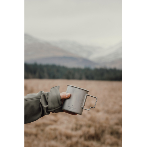 Personne tenant une tasse en titane en extérieur, sans personnalisation visible.