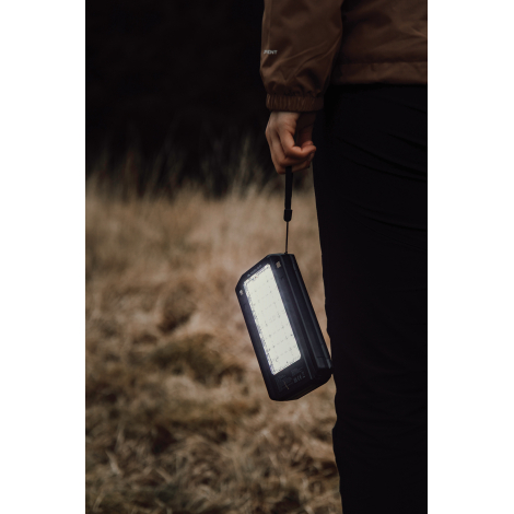 Personne tenant une powerbank allumée à la main en extérieur, sans marquage visible.