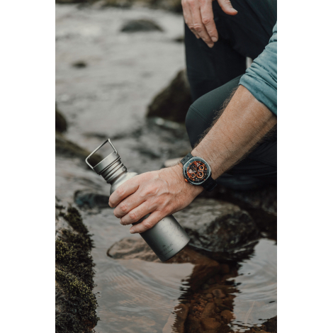 Montre connectée portée au poignet d’un homme tenant une gourde en extérieur, sans marquage visible.