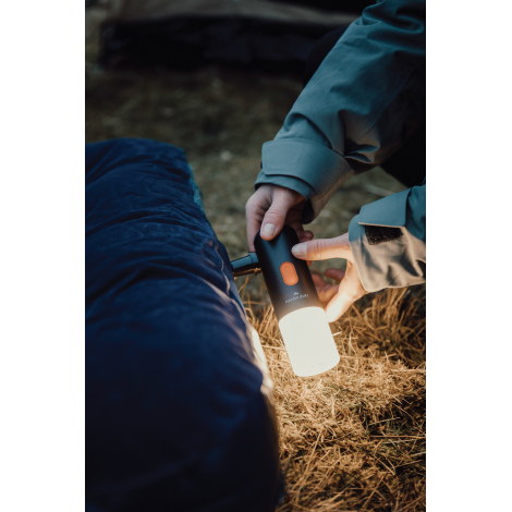 Lampe de camping utilisée en extérieur près d’un sac de couchage avec éclairage actif, sans personnalisation visible.