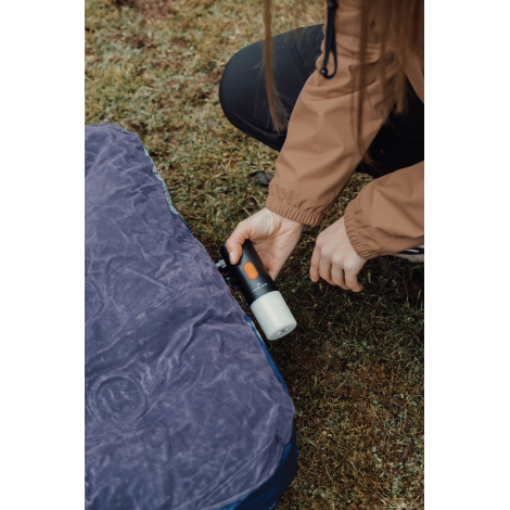 Lampe de camping manipulée par une personne près d’un tapis de sol en extérieur, sans personnalisation visible.