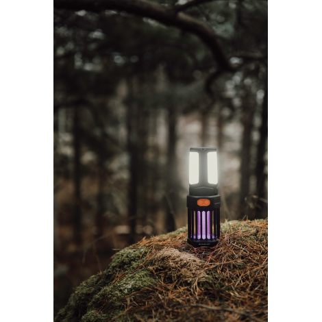 Lampe de camping éclairée posée sur un rocher en extérieur avec environnement forestier, sans marquage visible.