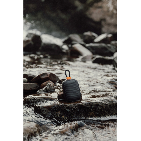 Enceinte posée sur des pierres en extérieur avec eau en arrière-plan, sans marquage visible.