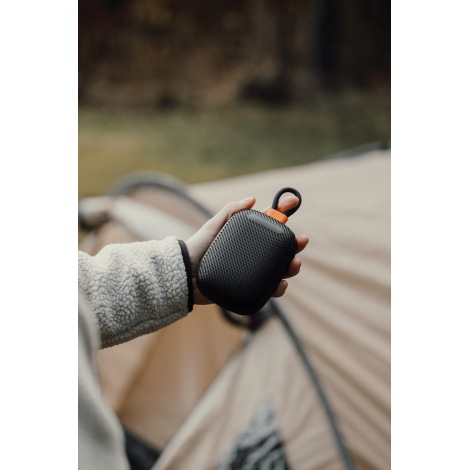 Enceinte tenue en main près d’une tente en extérieur, sans personnalisation visible.