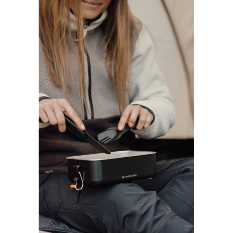 Personne utilisant un set de couverts en extérieur au-dessus d’un récipient, sans personnalisation visible.