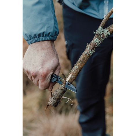 Personne utilisant un couteau pliant pour couper une branche en extérieur, sans personnalisation visible.
