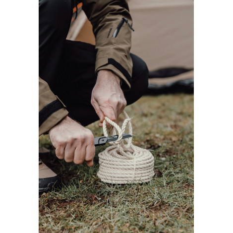 Personne utilisant un couteau pliant pour couper une corde en extérieur, sans marquage visible.