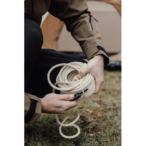 Porte-clés multifonctions utilisé pour couper une corde en extérieur, sans marquage visible.