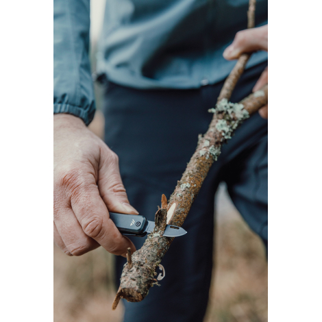 Porte-clés multifonctions utilisé pour couper une branche en extérieur, sans personnalisation apparente.
