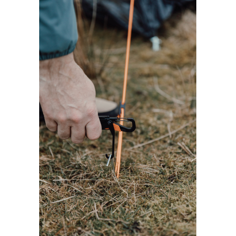 Outil multifonctions utilisé pour manipuler un piquet de tente au sol, sans personnalisation visible.