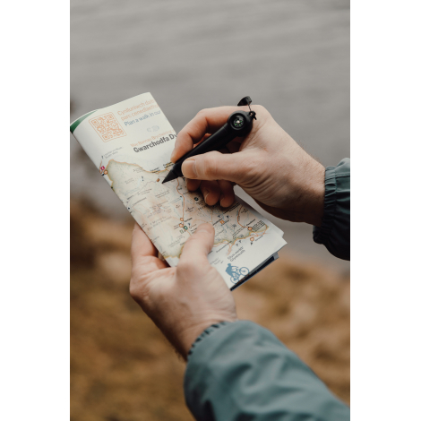 Personne utilisant un crayon infini pour écrire sur une carte en extérieur, sans marquage visible.