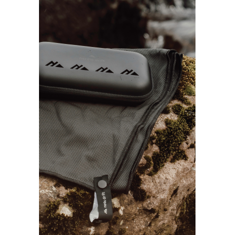 Serviette partiellement rangée dans une housse filet avec étui rigide posé dessus, sans marquage visible.