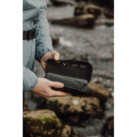 Serviette rangée dans un étui rigide tenue en main en extérieur, sans marquage visible.