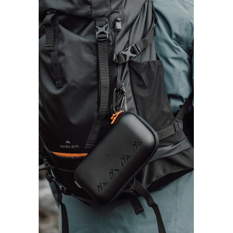 Étui rigide attaché à un sac à dos en extérieur, sans personnalisation visible.