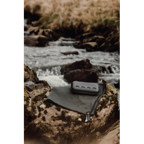 Serviette déployée au sol avec étui posé dessus en extérieur, sans personnalisation visible.