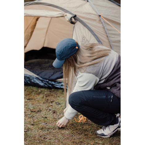 Casquette bleue portée par une femme accroupie près d’une tente en extérieur, sans marquage visible.