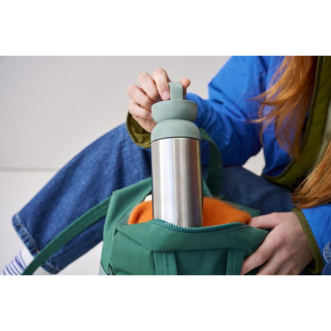 Personne tenant un mug isotherme avec partie supérieure verte partiellement dans un sac, sans personnalisation visible sur la zo