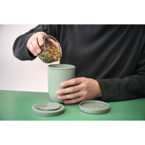 Personne manipulant un pot repas isotherme vert ouvert, sans marquage visible sur les surfaces observables.