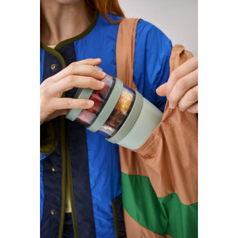 Personne tenant un pot repas isotherme vert avec compartiments partiellement dans un sac, sans marquage visible sur les zones vi