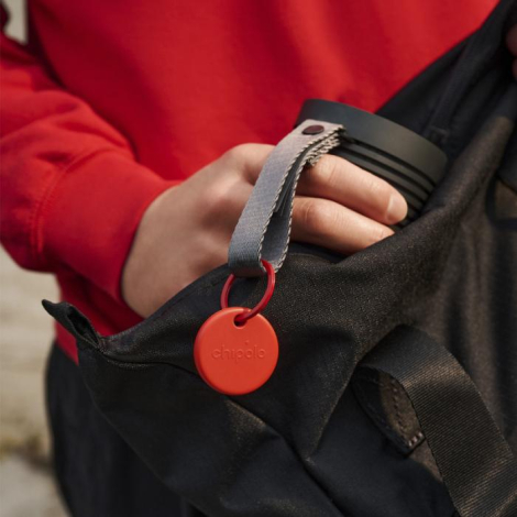 Balise de suivi rouge fixée à un sac avec anneau en situation, sans personnalisation apparente.